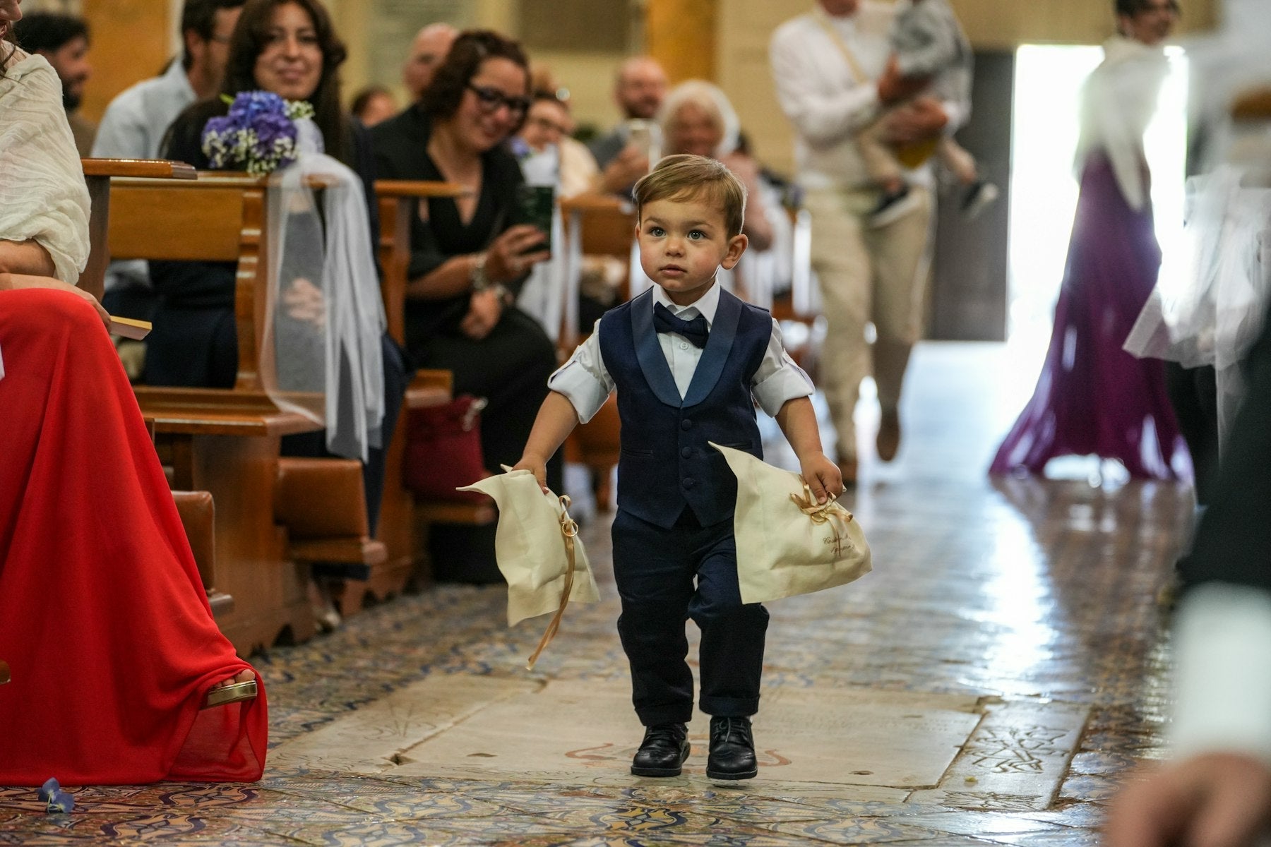 Young ring bearer in a suit walking down the wedding aisle